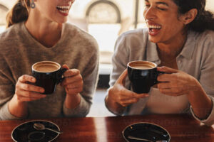 Two females sitting at a coffee table talking and laughing. Happy woman friends in a cafe having coffee.